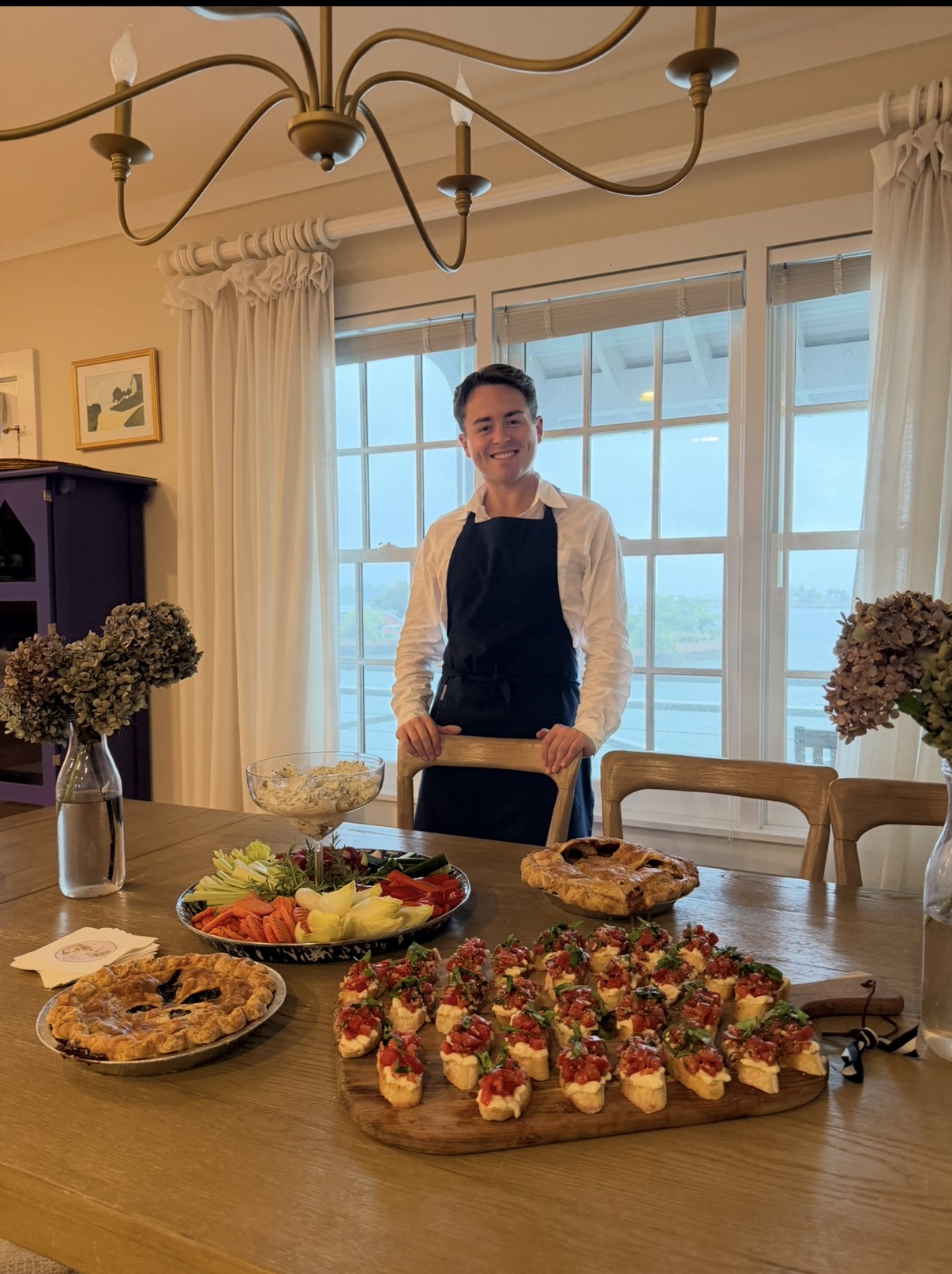 Sebastian standing behind a catered table of pies, vegetables and bruschetta